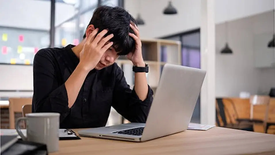 Stressed young man holding his head at a laptop, showing fatigue and burnout