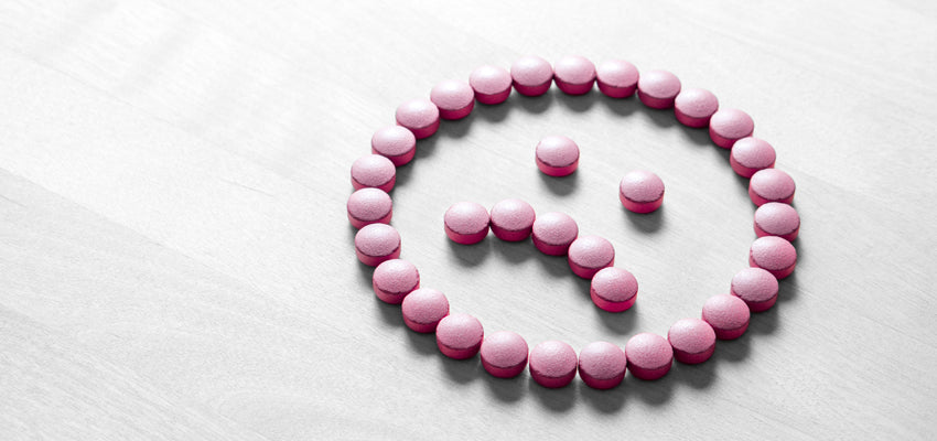 Pink pills arranged as a frowning face on a white surface