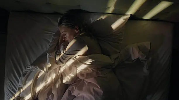 Woman sleeping peacefully in bed with soft morning light through the blinds