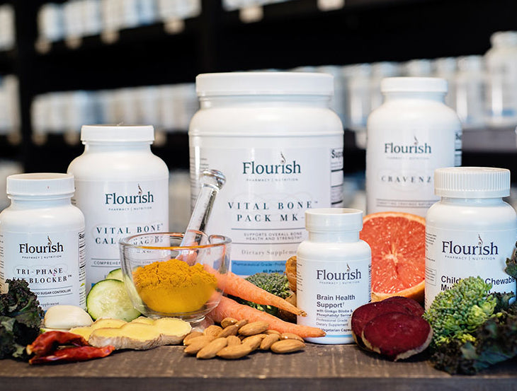 Assorted health products including bottles and containers with 'Flourish' branding on a table with fresh produce.