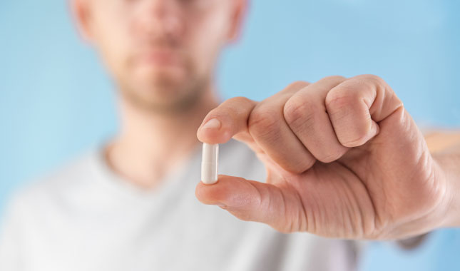 A person holds up a single supplement capsule